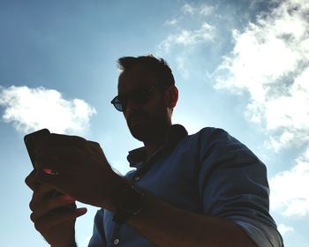 Low angle view of man using mobile phone against sky