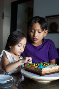 Cute siblings sitting by cake at home