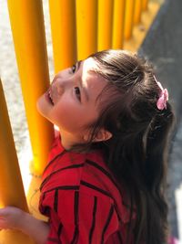 Close-up of thoughtful girl standing against yellow fence