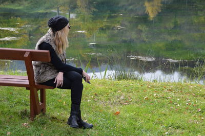 Side view full length of woman sitting on bench at grassy field