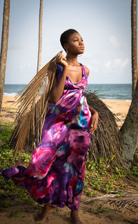 Young woman standing at beach against sky