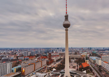 Fernsehturm against cityscape and cloudy sky