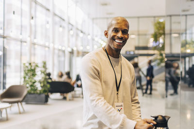 Portrait of happy male entrepreneur holding coffee pot while standing at convention center
