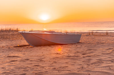 Boat moored on beach against sky during sunset