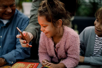 Cropped hand of woman showing mobile phone to family sitting at table