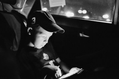 Boy wearing cap while using smart phone in car at night