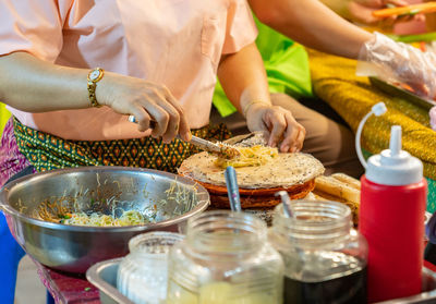 Woman's hand use pliers putting vermicelli on dough sheet for rolls in street food market.