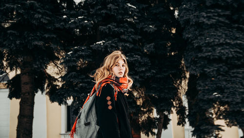 Portrait of young woman standing against trees in winter