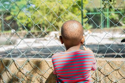 Rear view of boy standing by fence in zoo