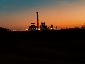 Silhouette factory against sky during sunset