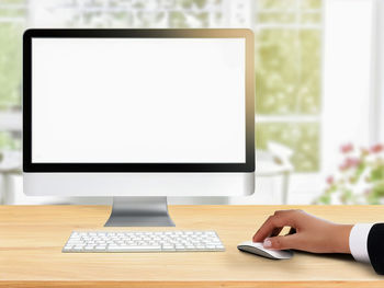 Hand working on computer with blurred window background inside house.