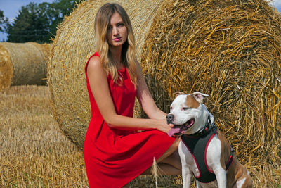 Portrait of young woman with dog by hay bale