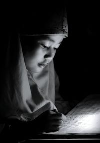 Close-up of girl wearing hijab studying in darkroom