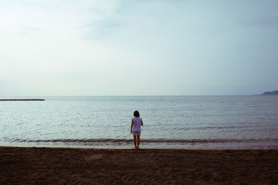 Rear view of boy standing on beach against sky