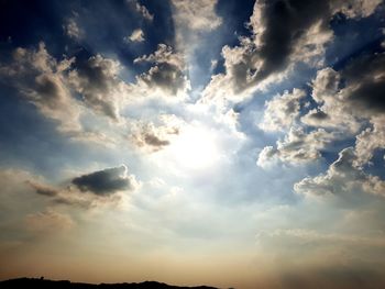 Low angle view of sunlight streaming through clouds