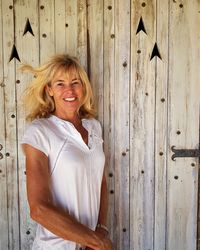 Portrait of smiling mature woman standing by wooden wall