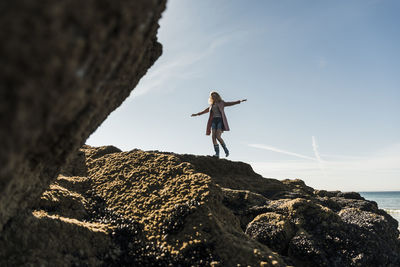 Woman standing on rock by sea against sky