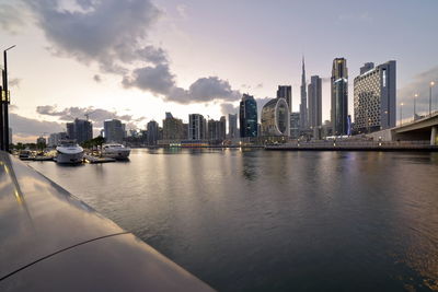 Modern buildings by river against sky in city