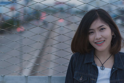 Portrait of young woman standing against chainlink fence