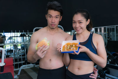 Portrait of couple holding fast food at gym