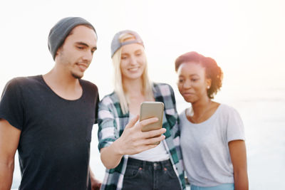 Portrait of young woman using mobile phone while standing against white background