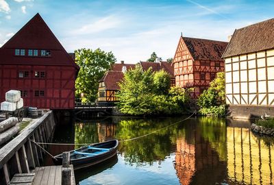 Rowboat moored at canal by old houses in town against sky