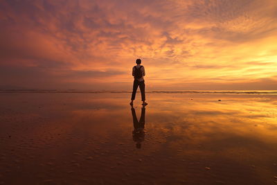 Man with umbrella standing on shore against dramatic sky