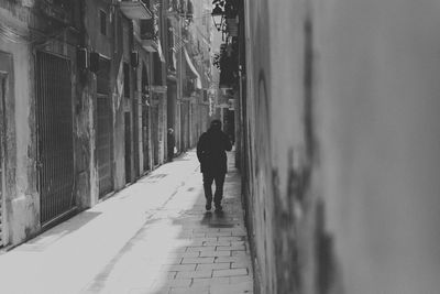 Rear view of man walking on footpath amidst buildings