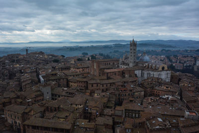 High angle view of siena cathedral and cityscape against cloudy sky