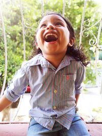 Close-up of smiling boy sitting by railing in balcony