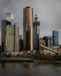 Modern buildings by river against sky in city