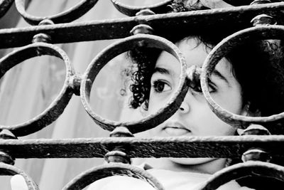Close-up of boy looking through metallic railing