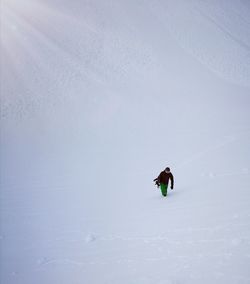 Lonely snowboarder climbing up snowcaped mountain