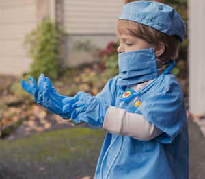 Boy in doctor costume wearing gloves while standing in yard