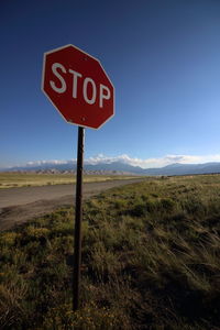 Road sign on field against clear blue sky