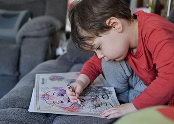 Cute young baby boy coloring pictures on the couch