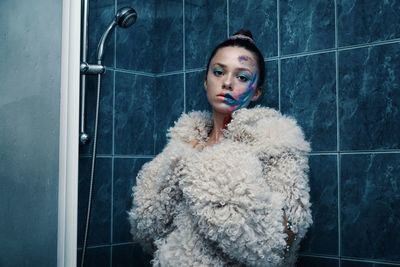 Portrait of woman with face paint wearing warm clothing in bathroom