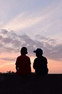 Rear view of silhouette man sitting against sky during sunset