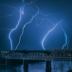 Lightning over illuminated bridge against sky at night