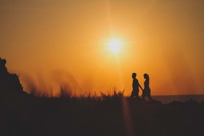 Silhouette man and woman on field against sky during sunset