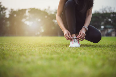 Low section of woman tying shoelace on grassy land