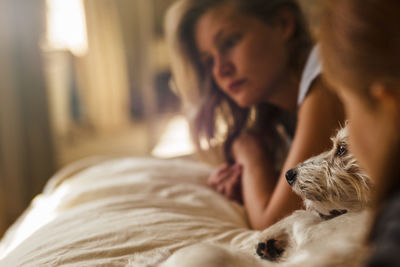 Close-up of girls and dog relaxing on bed