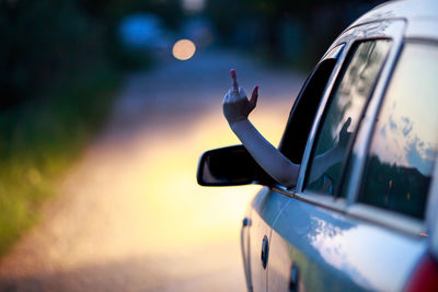 Cropped hand showing obscene gesture from car on road