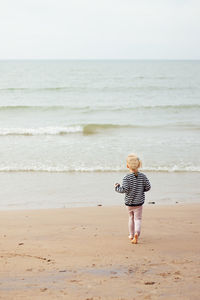Rear view of girl walking at beach against clear sky