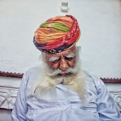Close-up of senior man with beard sitting by white wall