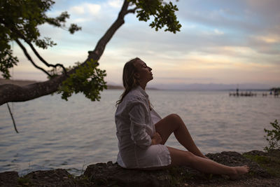 Woman sitting by tree against sky