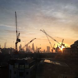 Cranes at construction site against sky during sunset