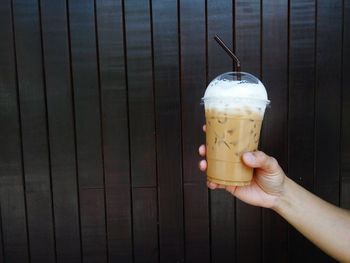 Cropped hand of woman holding iced coffee against wall