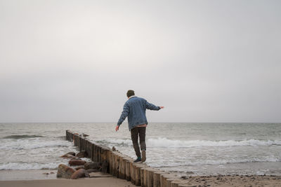 Rear view of man standing on beach against sky