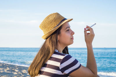 Young woman using mobile phone at beach against sky